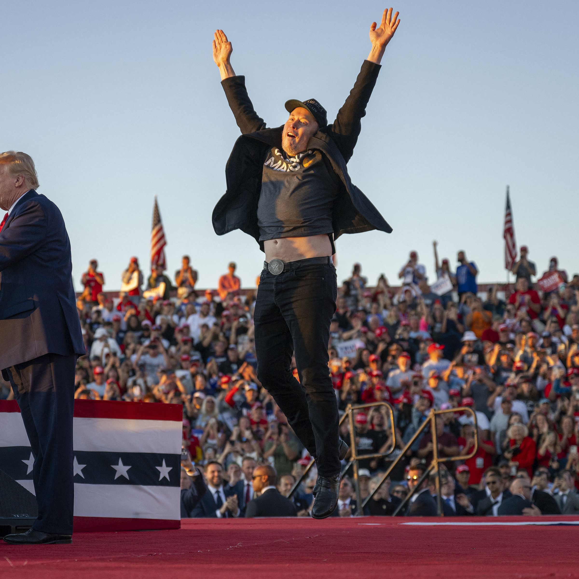 Tesla CEO Elon Musk (R) jumps on stage as he joins former US President and Republican presidential candidate Donald Trump during a campaign rally at site of his first assassination attempt in Butler, Pennsylvania on October 5, 2024.