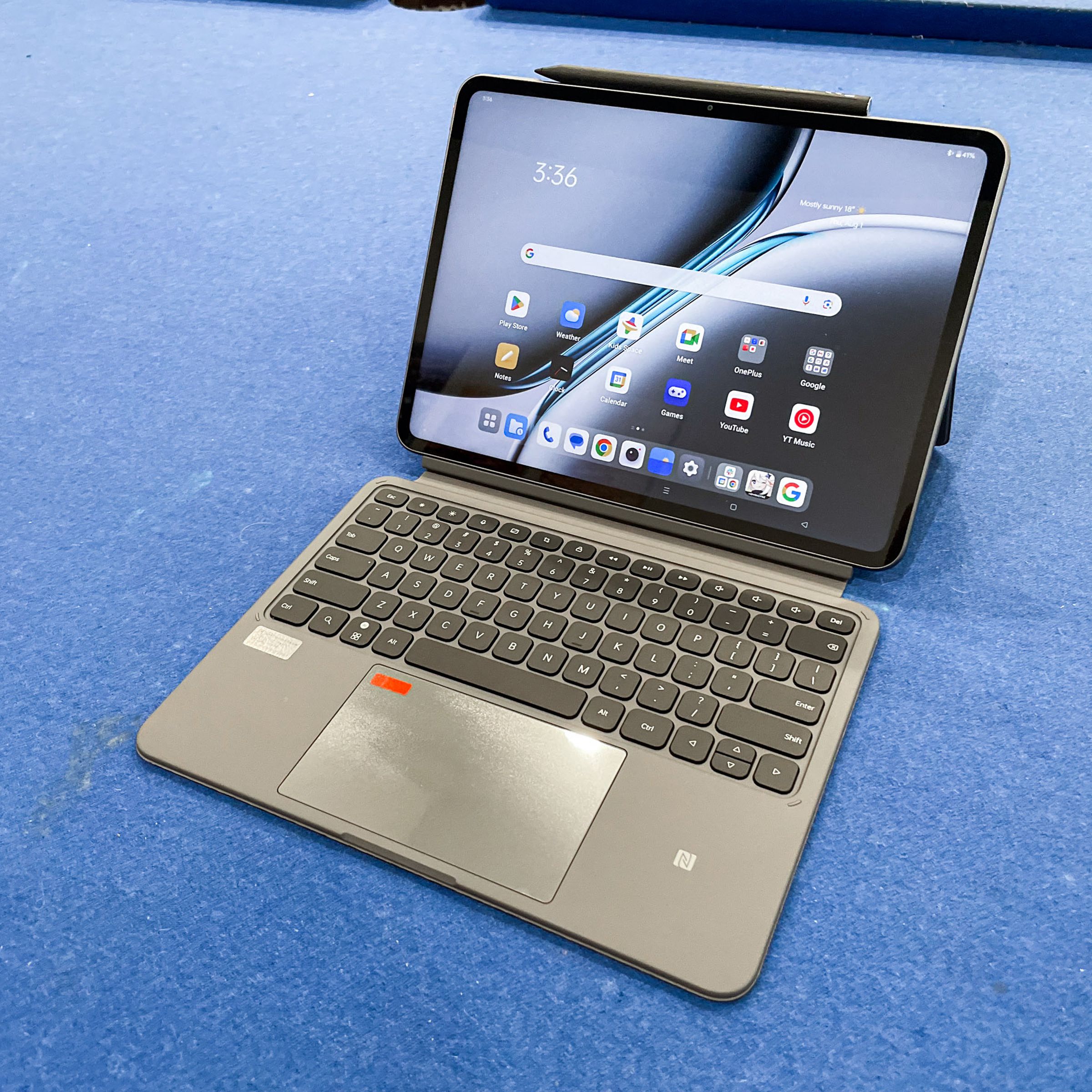 A OnePlus Pad 2 tablet on a blue surface with its stylus and smart keyboard case attached.