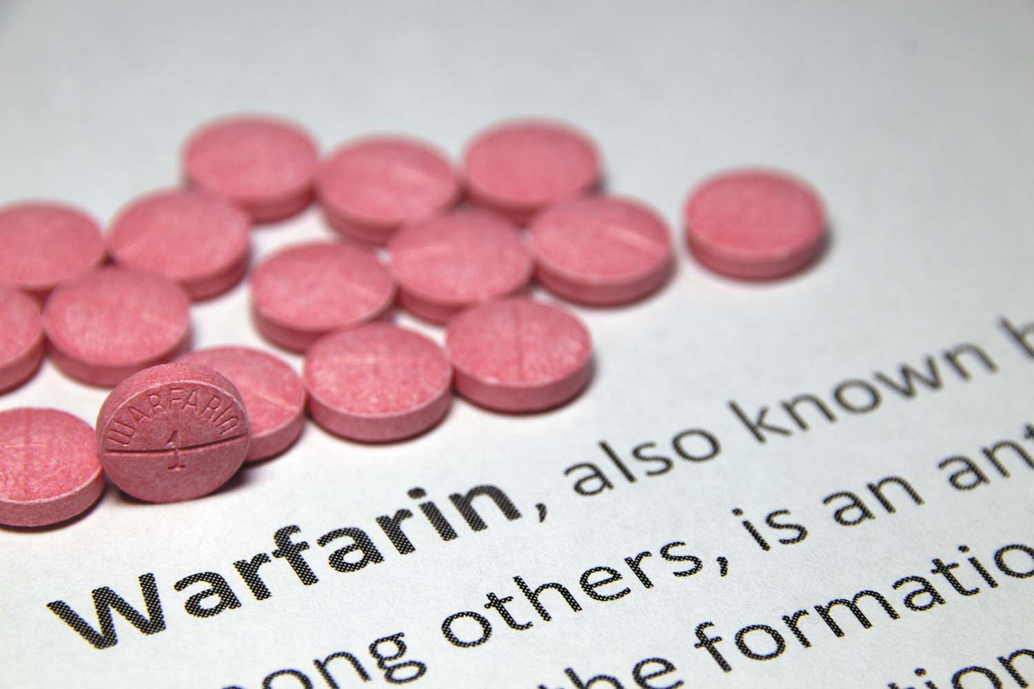 close-up photo of a batch of pink pills on a piece of paper with the definition of warfarin printed on it