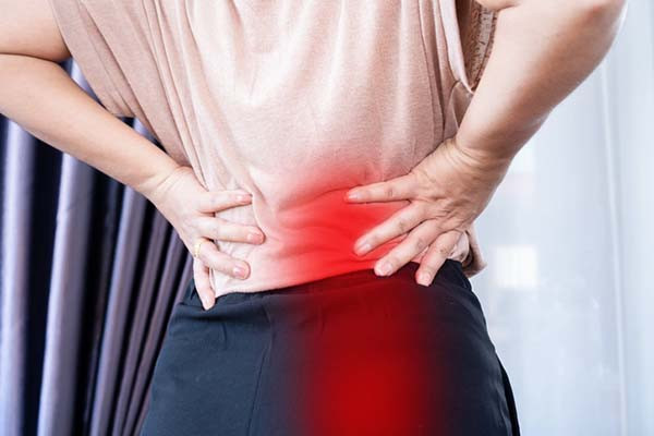 Cropped image of a woman's torso viewed from behind; her hands are on her hips with the fingers pointing toward her back, and there is a red glow superimposed on the image to represent sciatica pain.