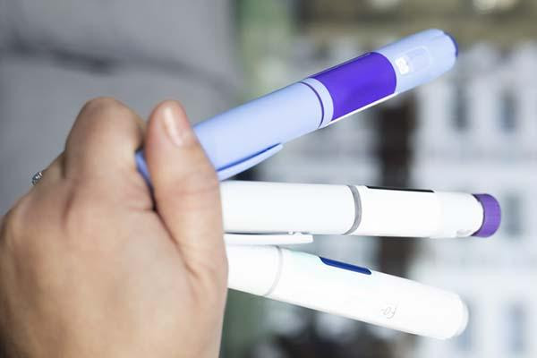 A hand holds three injector pens like those used for semaglutide-based medications for diabetes and weight loss.