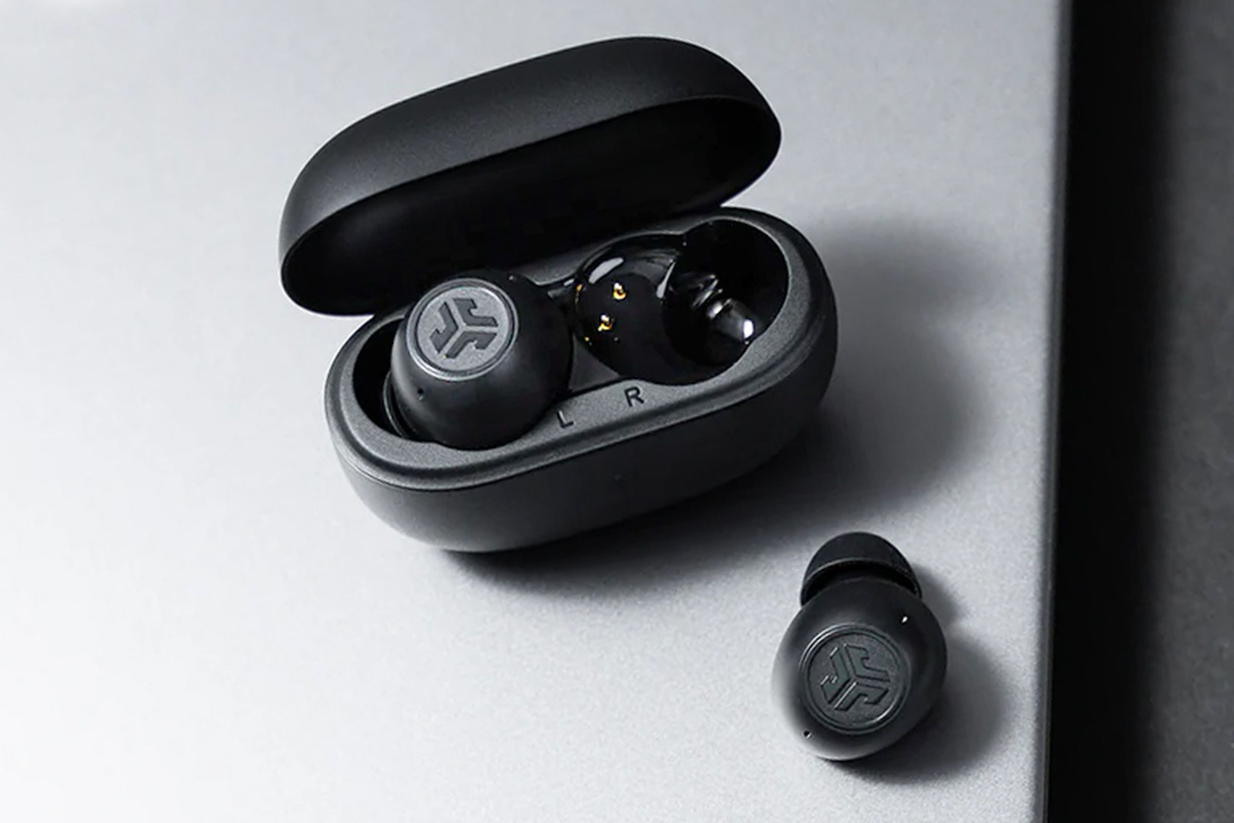 The JLab Go Pop ANC wireless earbuds sitting on a laptop with their charging case opened and a single earbud removed.