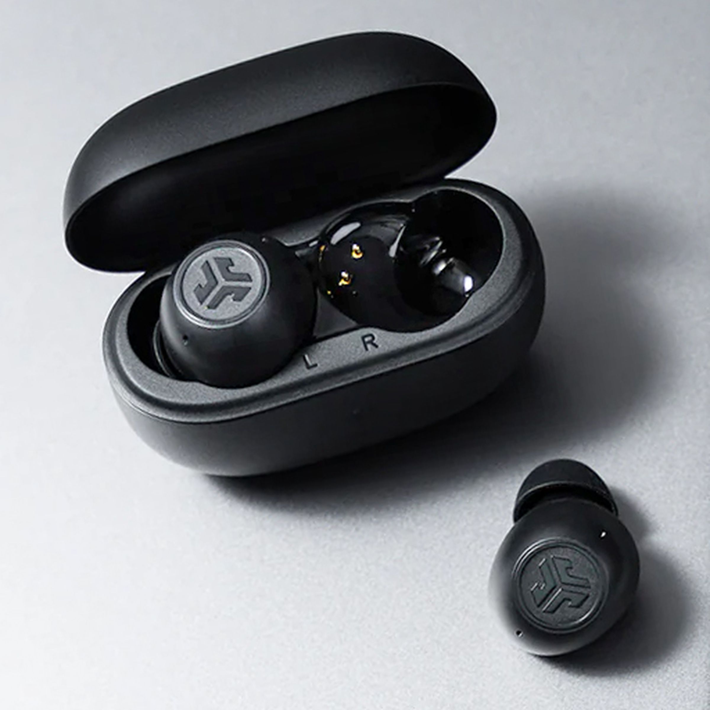 The JLab Go Pop ANC wireless earbuds sitting on a laptop with their charging case opened and a single earbud removed.