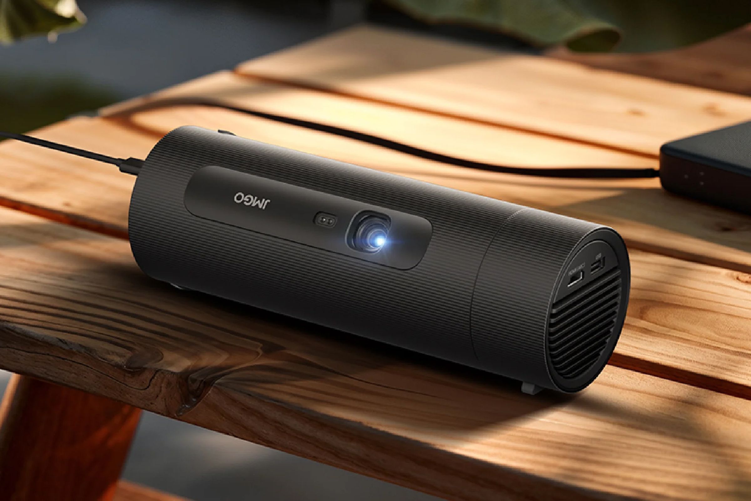 The JMGO Picoflix projector on a wooden picnic table plugged into a battery.