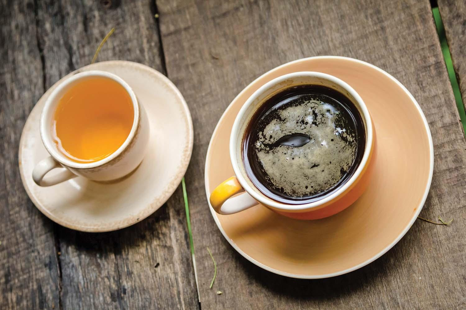 A cup of tea and a cup of coffee next to each other on a wood table.