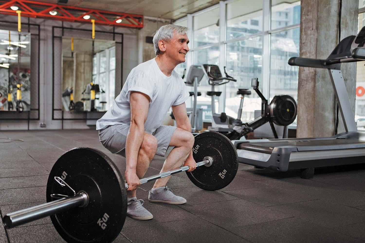 A man in a gym crouched behind a barbell, about to perform a dead lift.
