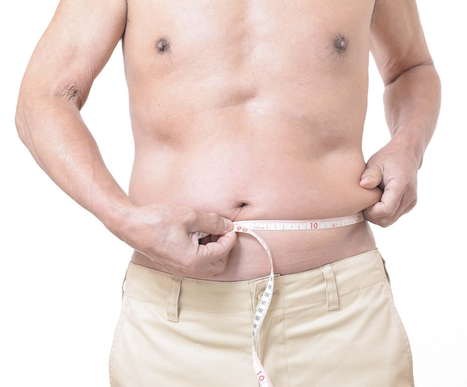 Cropped image showing the torso and arms of a shirtless man using a tape measure to check his waist circumfirence.