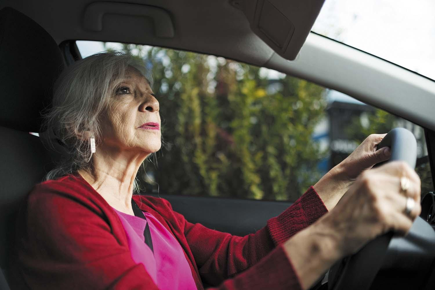 A senior woman driving, looking at the rear view mirror.