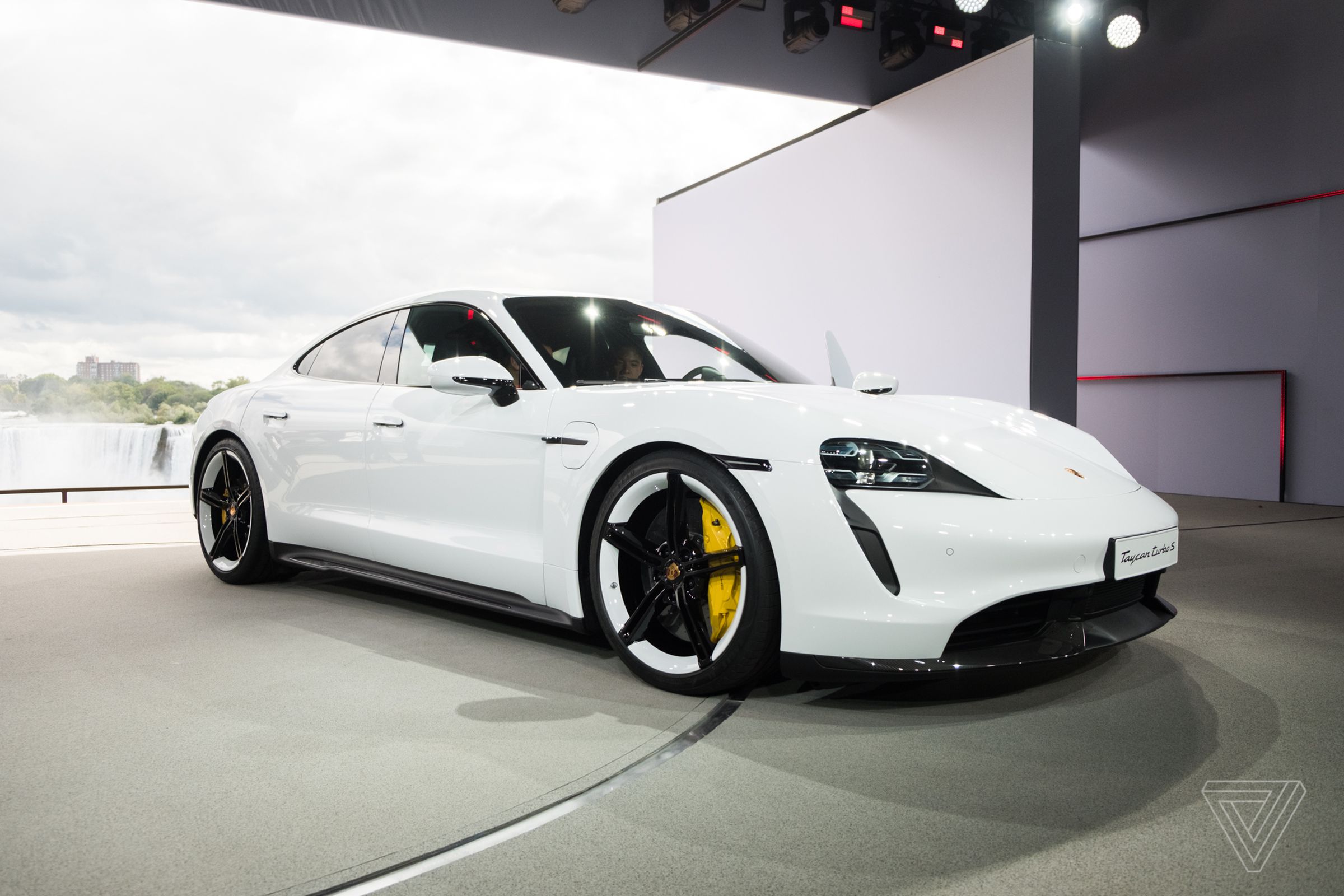 A photograph of a white Porsche Taycan parked in an open doorway.