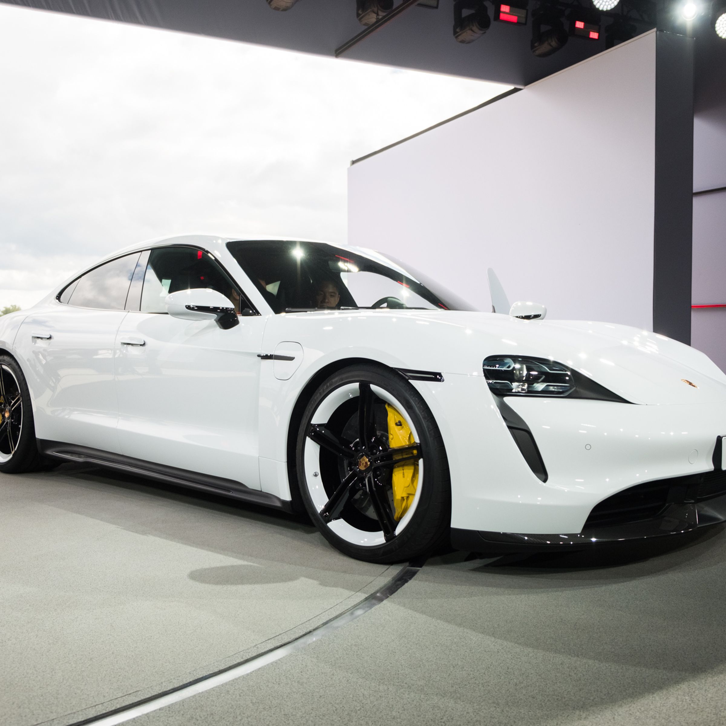 A photograph of a white Porsche Taycan parked in an open doorway.