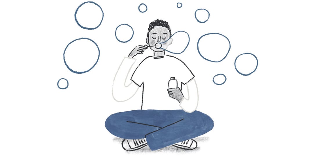 An illustration of a young man sitting cross-legged on the ground, blowing bubbles through a bubble wand.